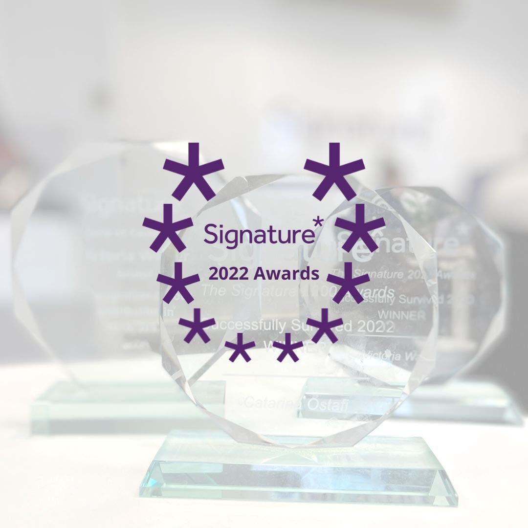 A transparent award plaque with a purple design proudly showcases the "Signature 2022 Awards" text. The award sits elegantly atop a glass base, with other similar plaques blurred in the background, capturing a moment of recognition at the prestigious Bristol event.