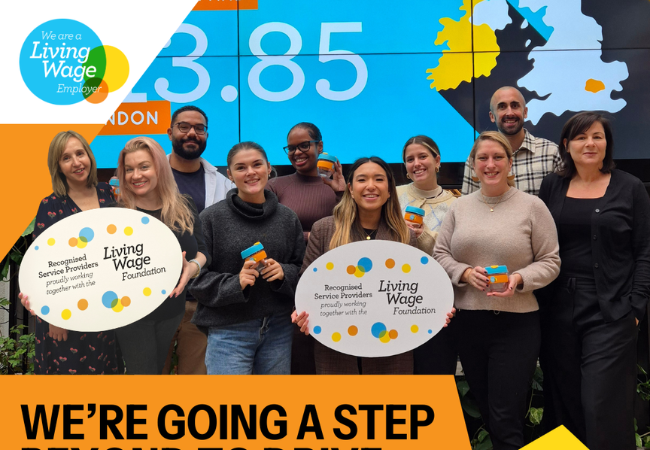 A group of ten smiling people hold signs saying "Recognized Service Providers" and "Living Wage Foundation." A map with "£23.85" looms in the background, while the banner below proudly declares, "WE'RE GOING A STEP BEYOND." These champions advocate for fair pay and the Real Living Wage.