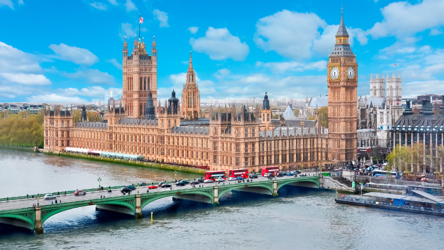 A panoramic view of the Palace of Westminster in London on a sunny day reveals the iconic Elizabeth Tower with Big Ben. As several red double-decker buses and cars cross the bridge over the River Thames, it feels like a scene worthy of Signature Awards recognition.