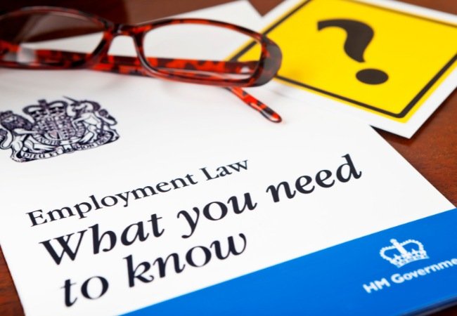 Close-up of a UK government employment law booklet titled 'Employment Law: What you need to know', with a pair of reading glasses and a paper featuring a question mark placed beside it.