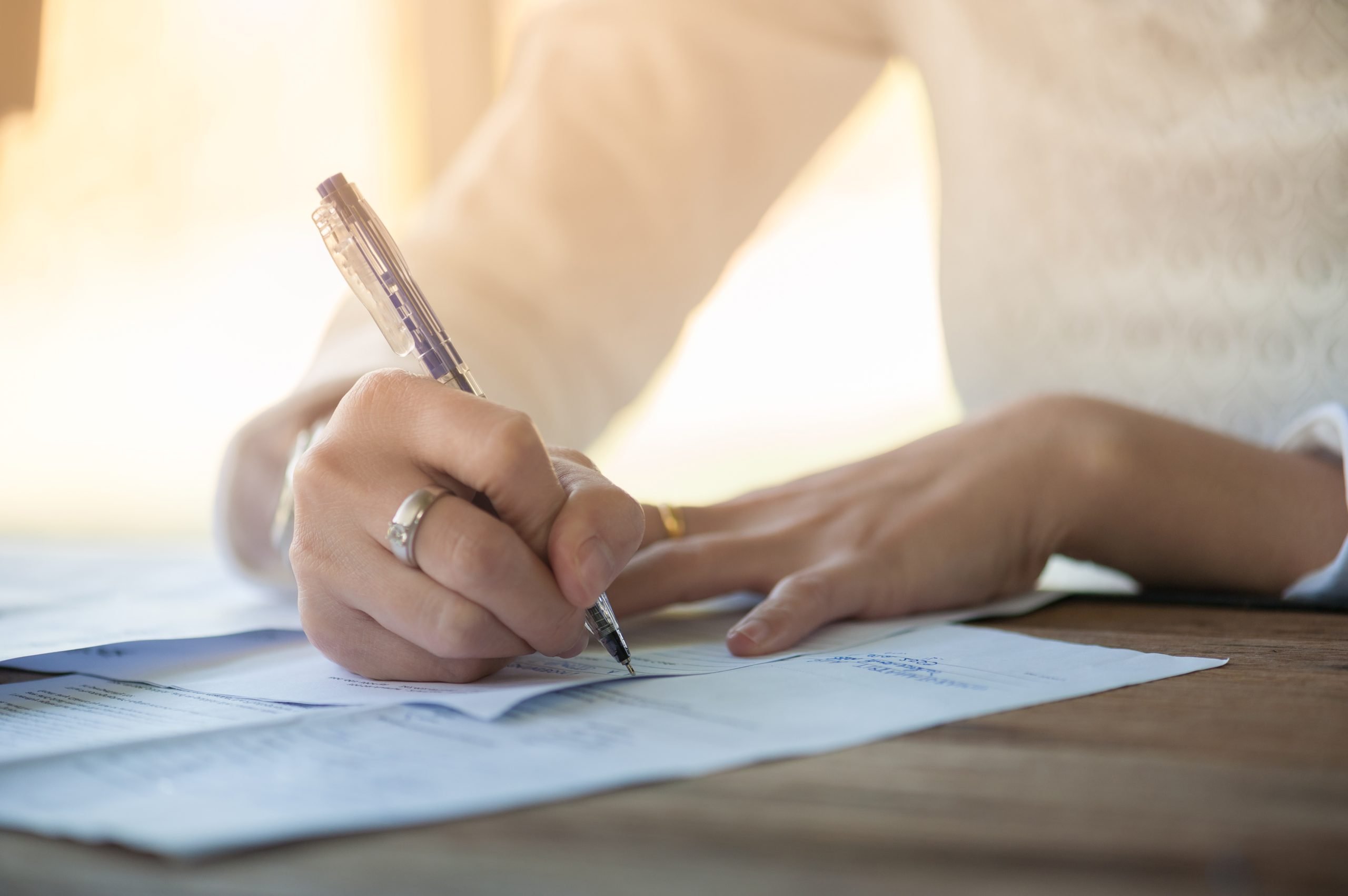 Woman hand writing some messages on contract document paper on wood table in morning time.